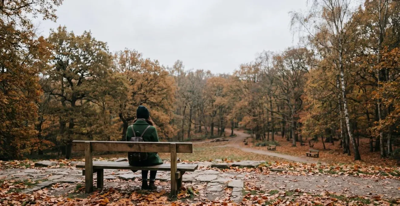 Femme assise seule sur un banc de parc en automne, vue de dos, environnement paisible mais mélancolique