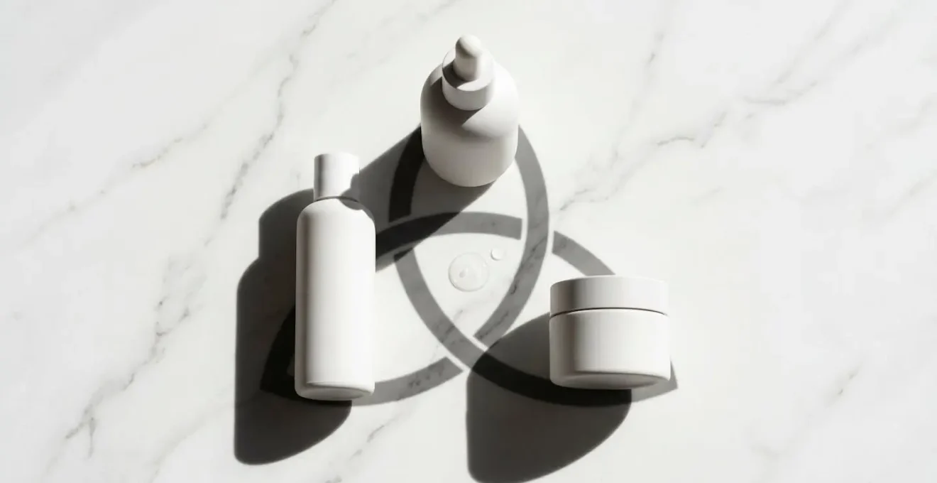 Trois flacons de soins cosmétiques épurés disposés en triangle sur une surface en marbre